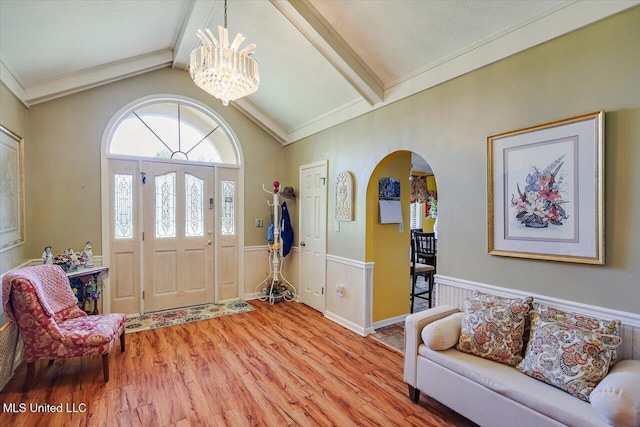 foyer with vaulted ceiling with beams, a wainscoted wall, arched walkways, light wood-style flooring, and a notable chandelier