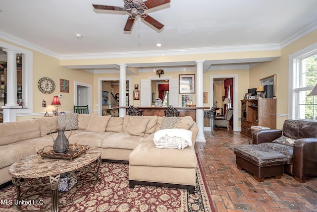 living area featuring ornate columns, ceiling fan, ornamental molding, and brick floor