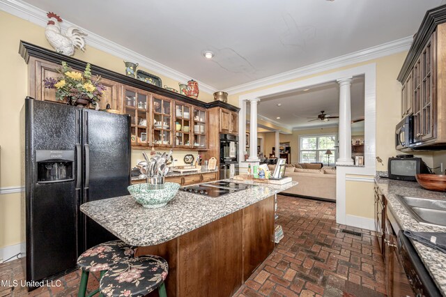 kitchen with decorative columns, black appliances, a kitchen island, baseboards, and brick floor