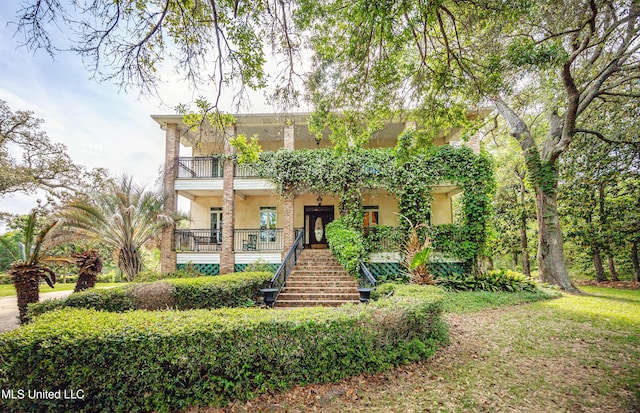 view of front of house with stucco siding, stairway, and a balcony