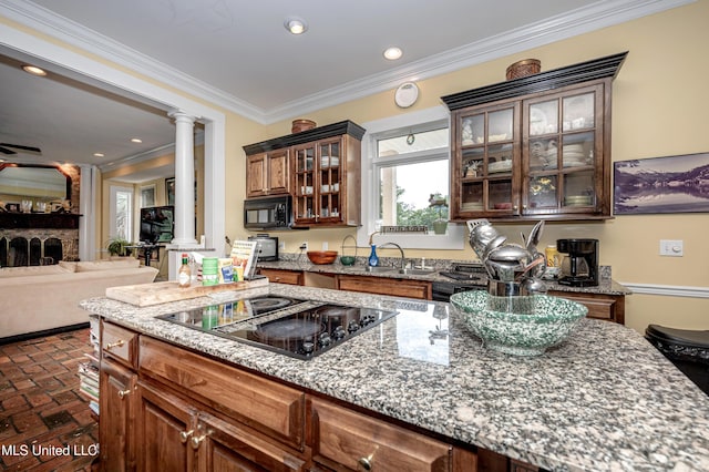 kitchen featuring light stone counters, crown molding, a sink, black appliances, and ornate columns