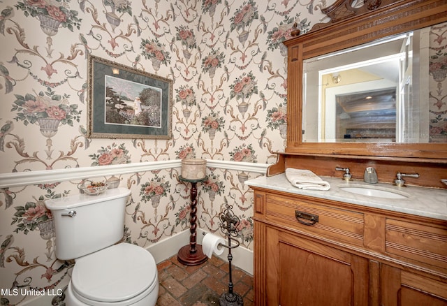 bathroom featuring vanity, toilet, wallpapered walls, and baseboards