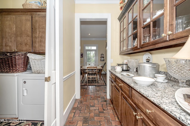 clothes washing area featuring brick floor, cabinet space, baseboards, washer and clothes dryer, and crown molding