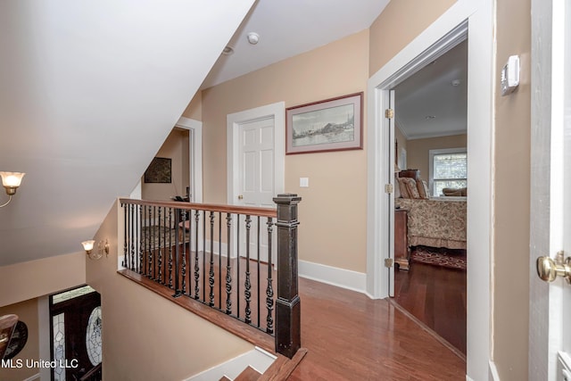 corridor with baseboards, wood finished floors, and an upstairs landing