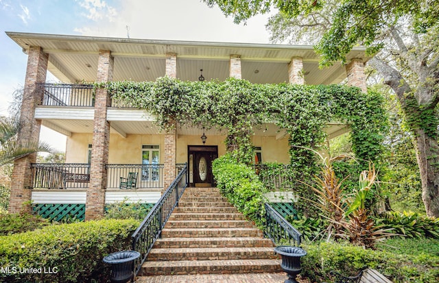 view of front of property with stairway, stucco siding, covered porch, and a balcony