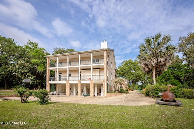 back of property with a chimney, a balcony, and a lawn