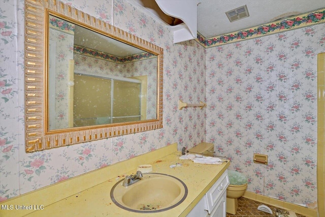 bathroom featuring vanity, toilet, a shower with door, and a textured ceiling