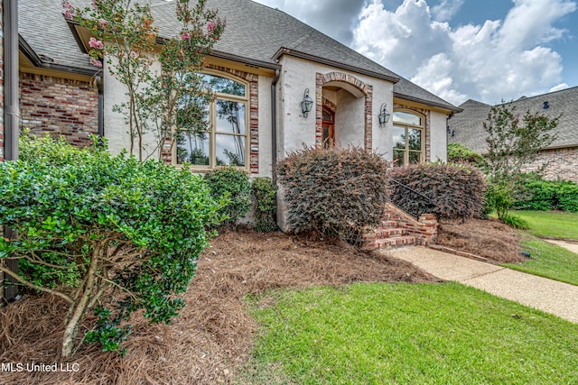 french country style house featuring a shingled roof and brick siding