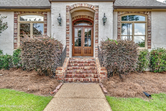 property entrance featuring french doors, roof with shingles, and stucco siding