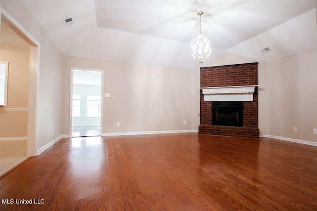 unfurnished living room with a brick fireplace, wood-type flooring, lofted ceiling, and an inviting chandelier