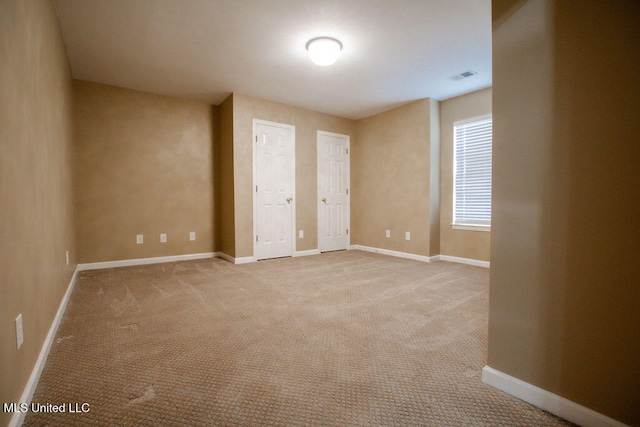 unfurnished bedroom featuring light carpet and two closets