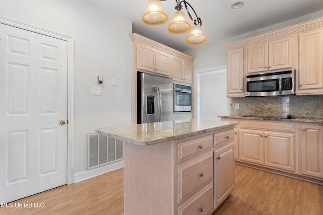 kitchen featuring appliances with stainless steel finishes, a kitchen island, backsplash, decorative light fixtures, and light hardwood / wood-style flooring