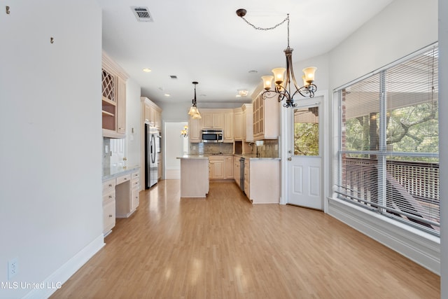 kitchen with appliances with stainless steel finishes, a kitchen island, light hardwood / wood-style floors, decorative light fixtures, and decorative backsplash