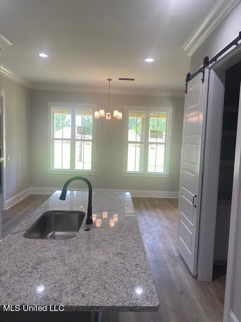 kitchen featuring wood-type flooring, sink, a barn door, hanging light fixtures, and crown molding