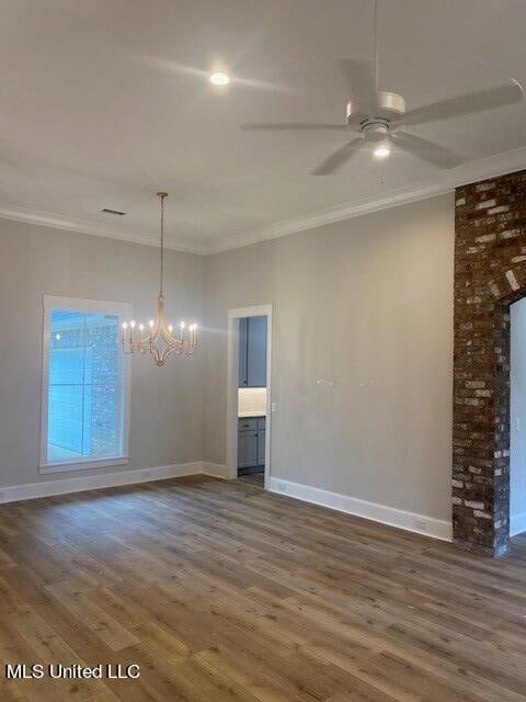 spare room featuring dark wood-type flooring, crown molding, and ceiling fan with notable chandelier