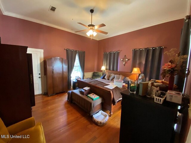 bedroom featuring ornamental molding, wood finished floors, visible vents, and a ceiling fan