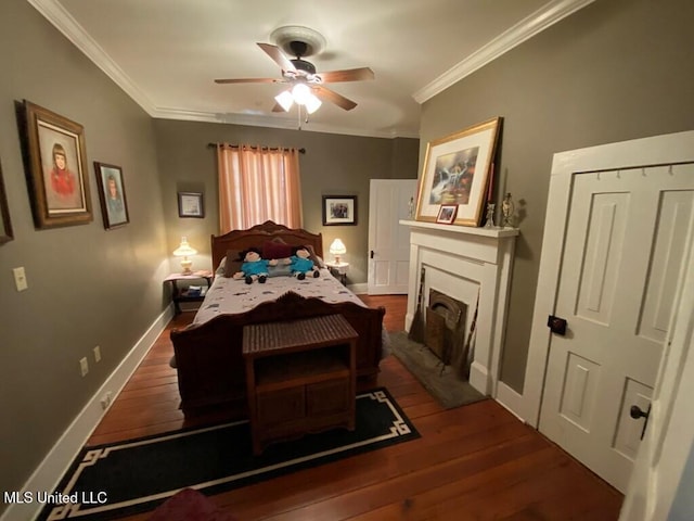 bedroom featuring a fireplace, crown molding, wood-type flooring, ceiling fan, and baseboards