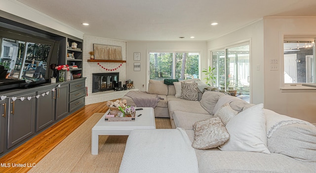 living area featuring a brick fireplace, light wood-style flooring, ornamental molding, and recessed lighting