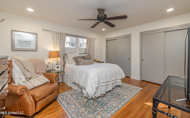 bedroom with recessed lighting, wood finished floors, a ceiling fan, multiple closets, and crown molding