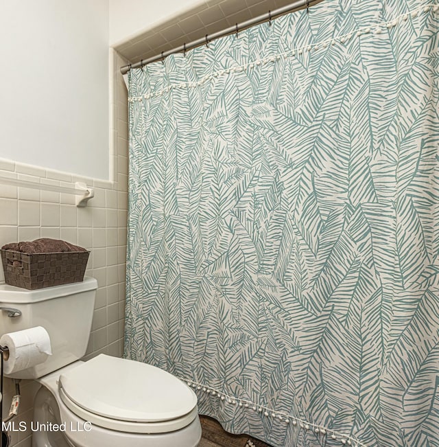 full bathroom with curtained shower, a wainscoted wall, tile walls, and toilet