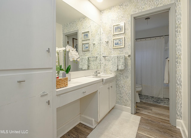 bathroom with toilet, wallpapered walls, wood finished floors, and vanity