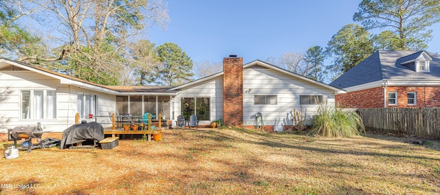 rear view of property featuring a sunroom, a chimney, fence, and a lawn