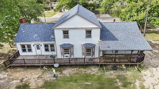 rear view of house featuring a deck, a chimney, and roof with shingles