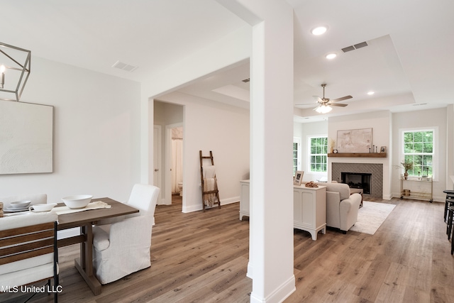 interior space with light wood-type flooring, a raised ceiling, and a tiled fireplace