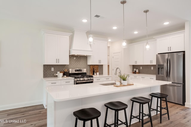 kitchen featuring a center island with sink, sink, custom range hood, appliances with stainless steel finishes, and white cabinetry