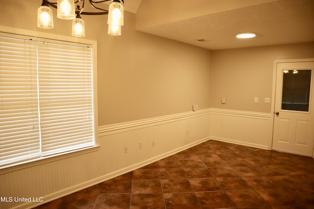 unfurnished room featuring a wainscoted wall, dark tile patterned flooring, a textured ceiling, and a chandelier