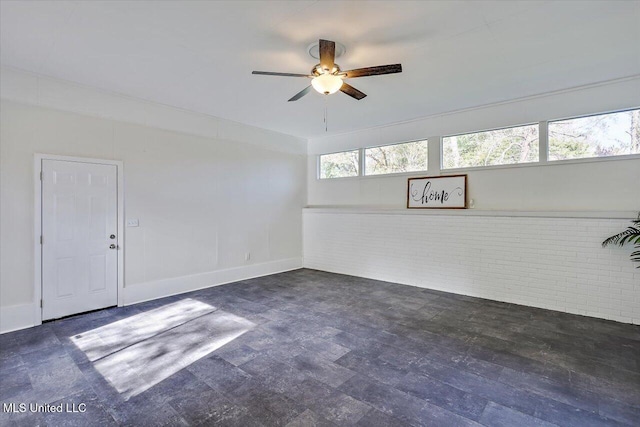 spare room featuring ceiling fan and brick wall