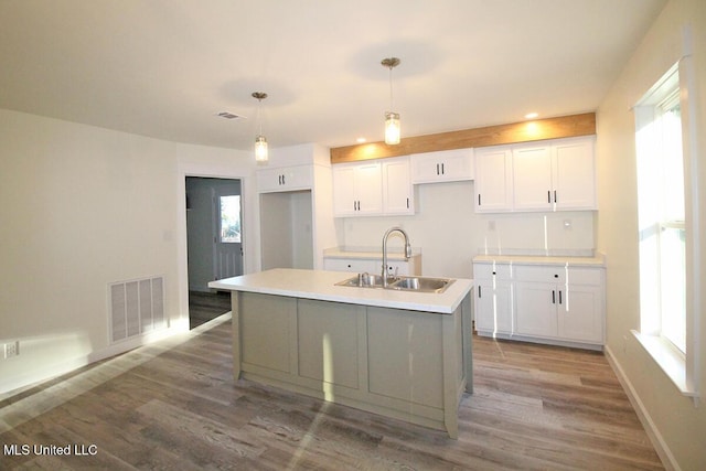 kitchen featuring sink, white cabinets, pendant lighting, and a center island with sink