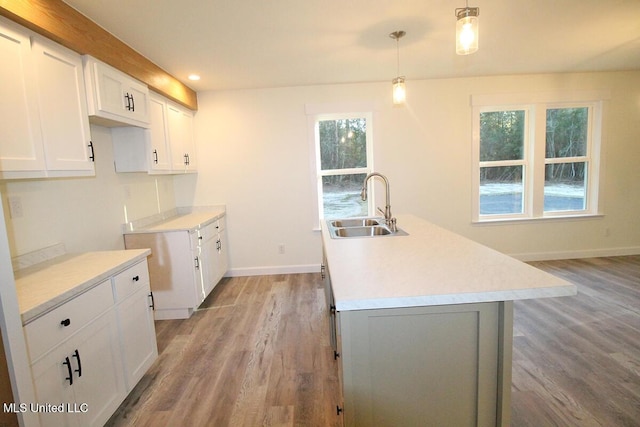 kitchen featuring a center island with sink, white cabinetry, sink, and hanging light fixtures