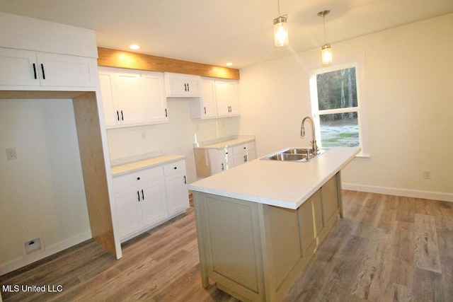 kitchen with a kitchen island with sink, sink, white cabinets, and decorative light fixtures