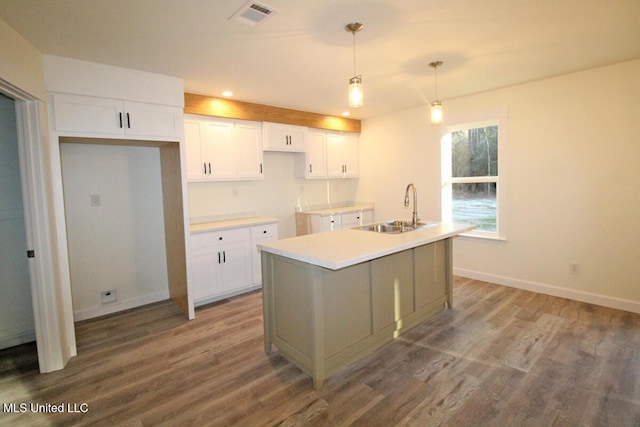 kitchen with a kitchen island with sink, sink, pendant lighting, light hardwood / wood-style floors, and white cabinetry