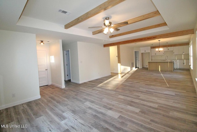 unfurnished living room with ceiling fan with notable chandelier, wood-type flooring, sink, and a tray ceiling