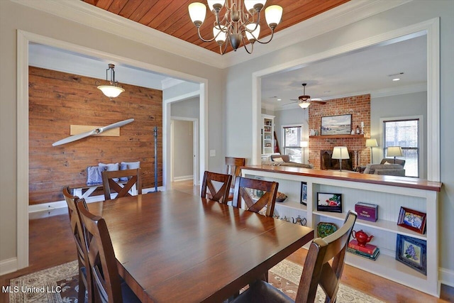 dining space featuring ornamental molding, wood finished floors, wooden walls, wooden ceiling, and a brick fireplace