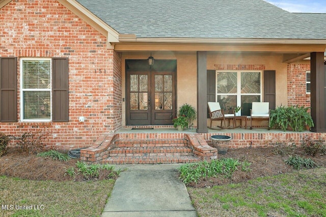 entrance to property with covered porch, french doors, brick siding, and a shingled roof