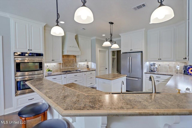 kitchen with backsplash, stainless steel appliances, custom exhaust hood, and visible vents