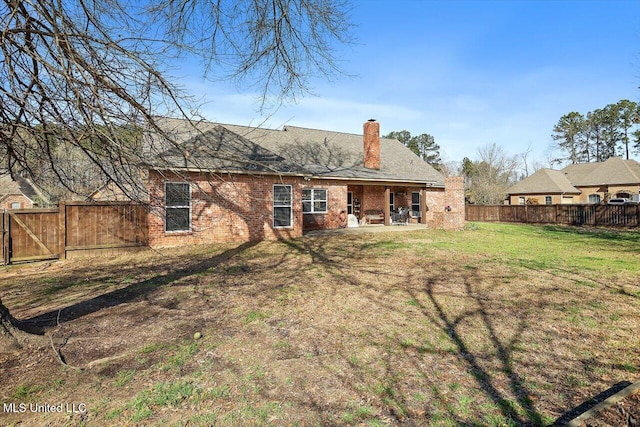 rear view of property with a fenced backyard, a yard, brick siding, a chimney, and a patio area