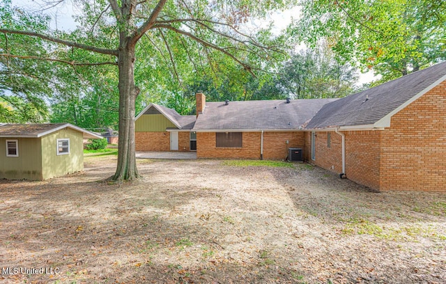 rear view of property featuring an outdoor structure, brick siding, central AC, a chimney, and a shingled roof
