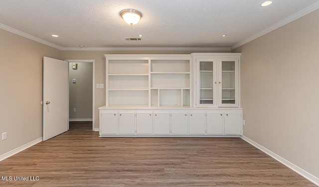 empty room featuring wood finished floors, ornamental molding, visible vents, recessed lighting, and baseboards