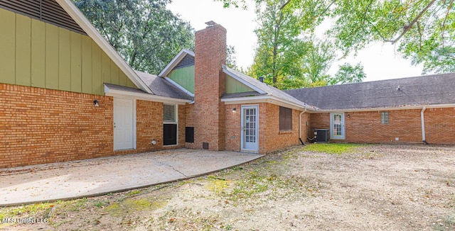 rear view of property with a chimney, a patio area, central AC unit, and brick siding