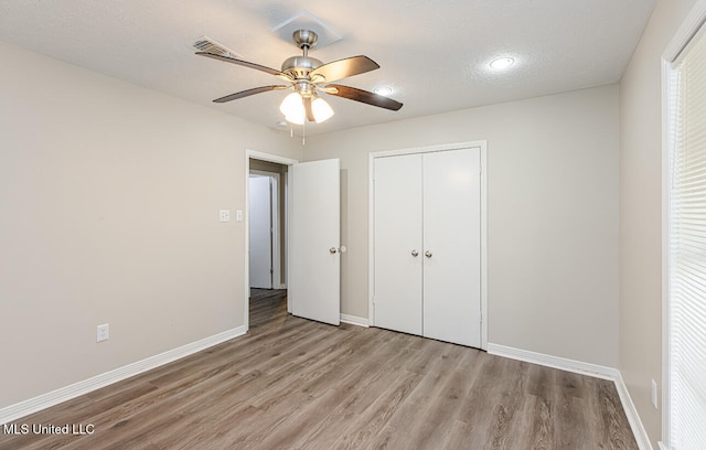 unfurnished bedroom featuring multiple windows, a closet, light hardwood / wood-style flooring, a textured ceiling, and ceiling fan