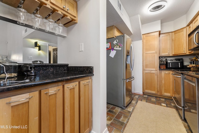 kitchen with appliances with stainless steel finishes, dark stone counters, brick floor, and visible vents