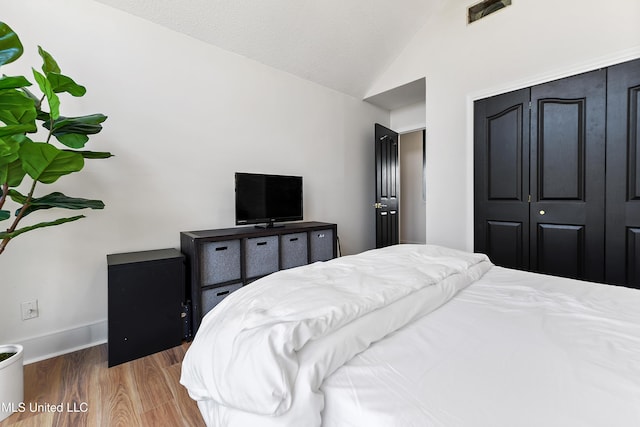 bedroom with lofted ceiling, wood finished floors, visible vents, baseboards, and a closet