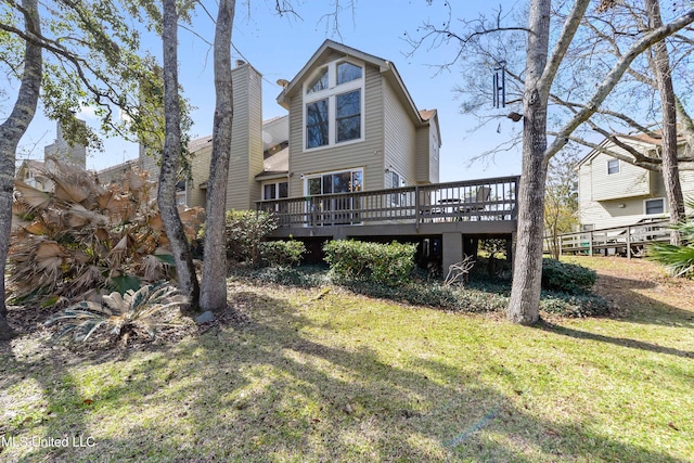 rear view of house with a chimney, a deck, and a lawn