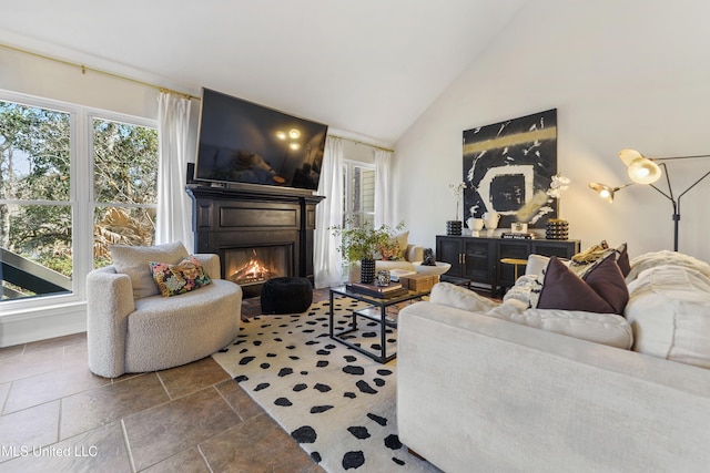 living area with high vaulted ceiling and a glass covered fireplace