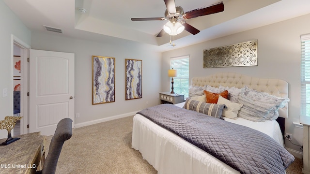 carpeted bedroom with a raised ceiling and ceiling fan