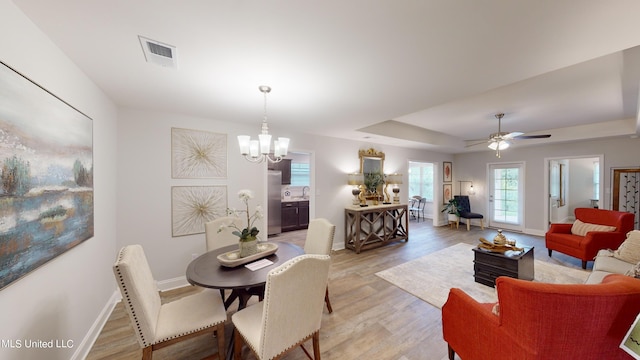 dining area featuring ceiling fan with notable chandelier, light hardwood / wood-style floors, and a raised ceiling